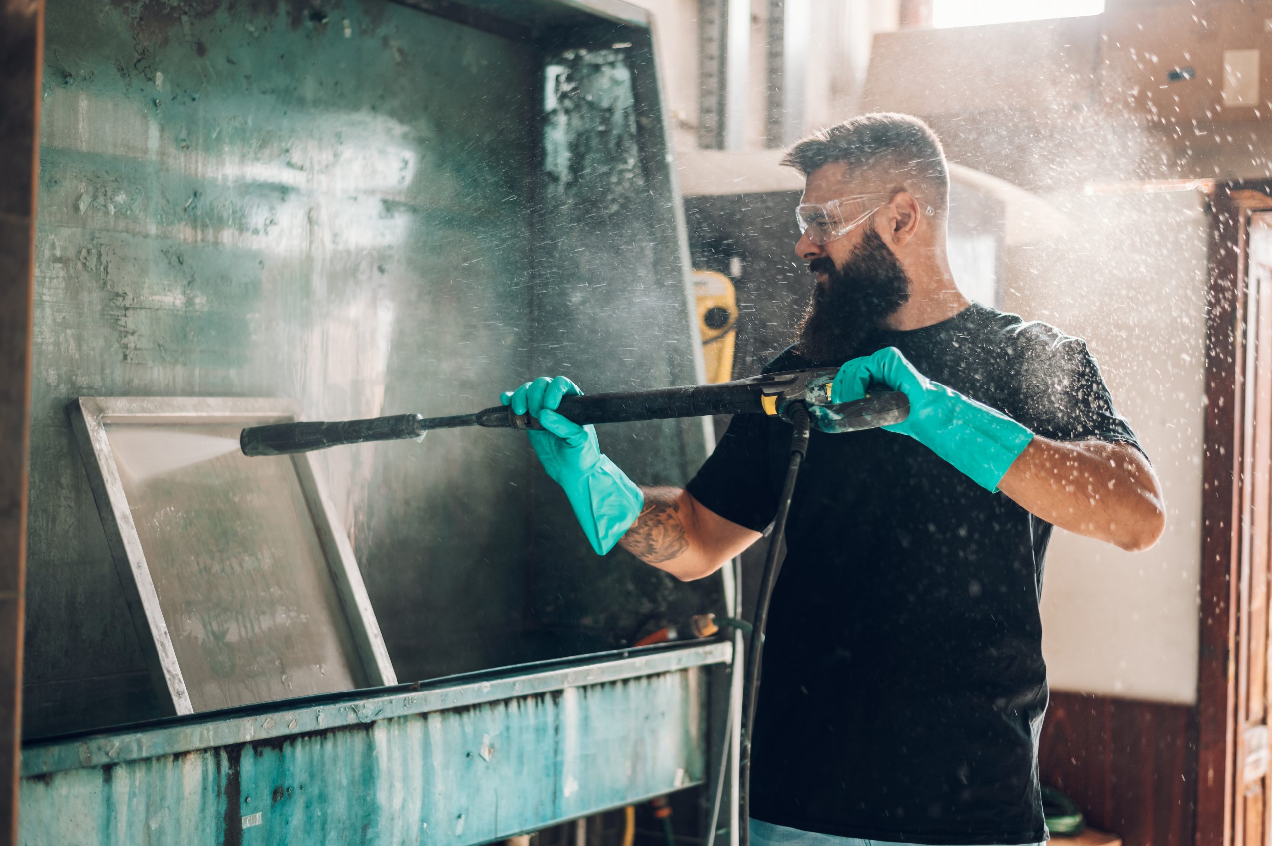 Male worker cleaning screen frame with water in a printing works Male worker cleaning screen frame with water in a printing works
